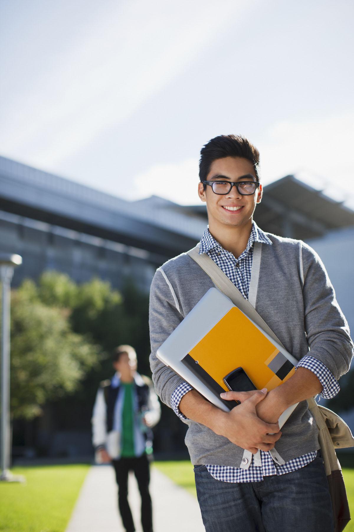 international student holds books and papers and smiles at the camera