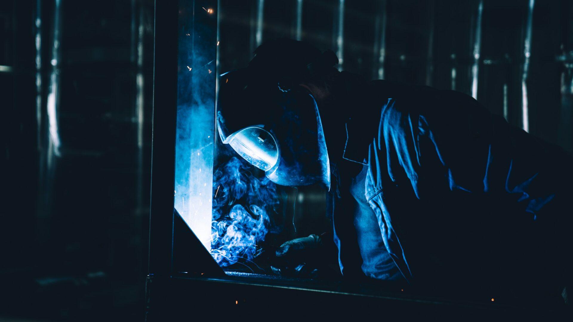 Welder in a black helmet in a dark room