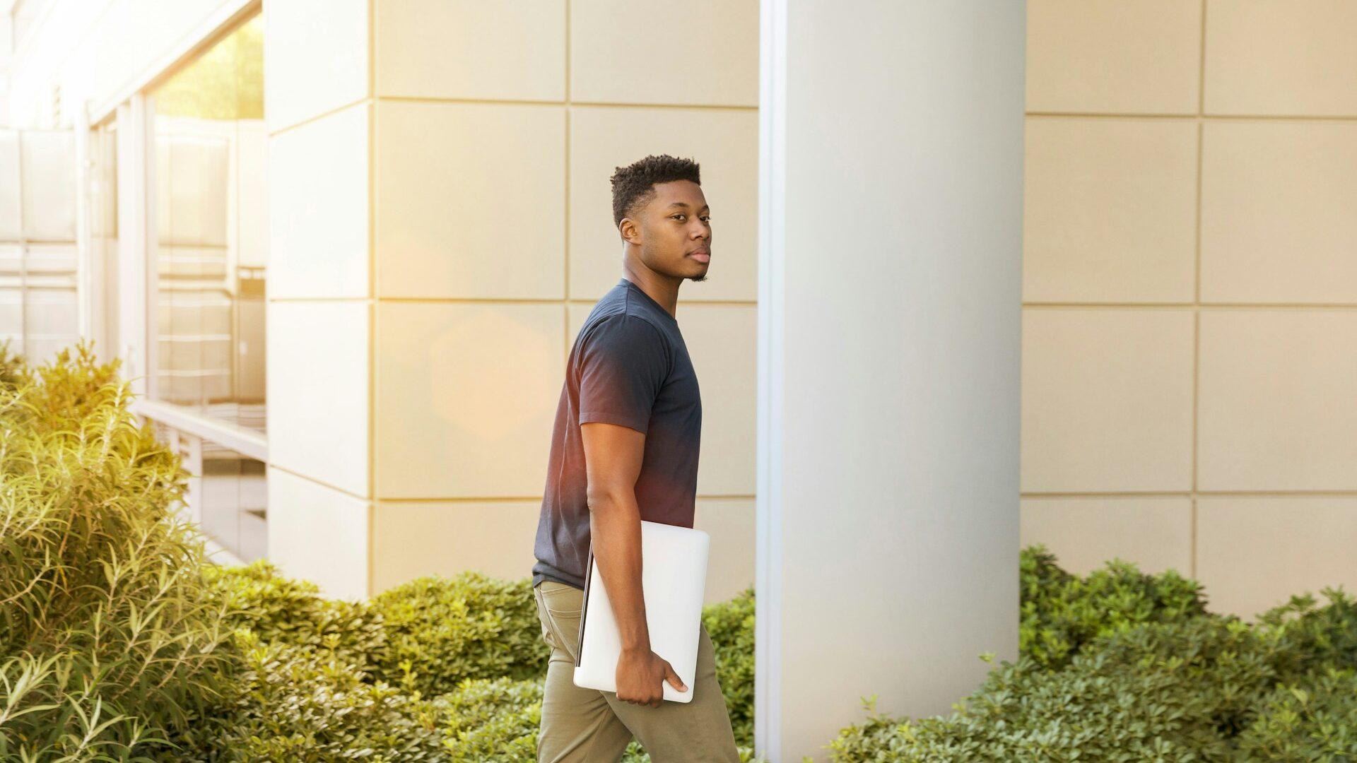 man holding laptop and walking into a campus building